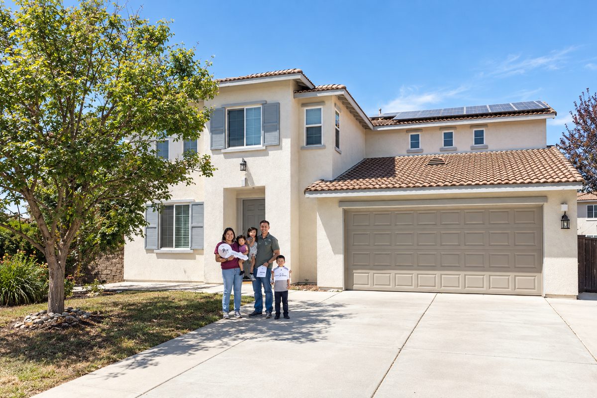 A family of five holding oversized keys and signs in front of their new two-story home on closing day