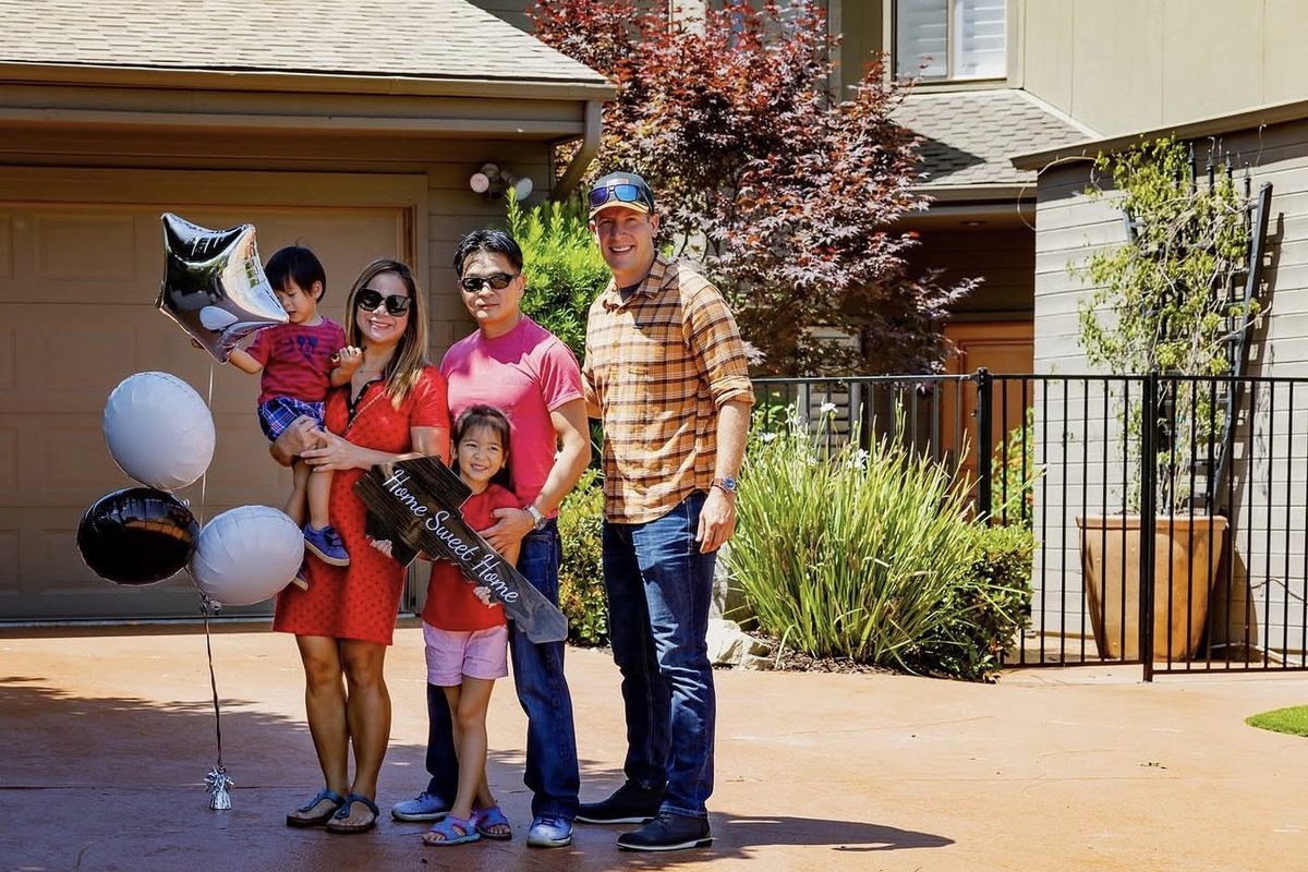 Stephen Resendes standing with a family of four holding balloons and a Home Sweet Home sign in their new driveway